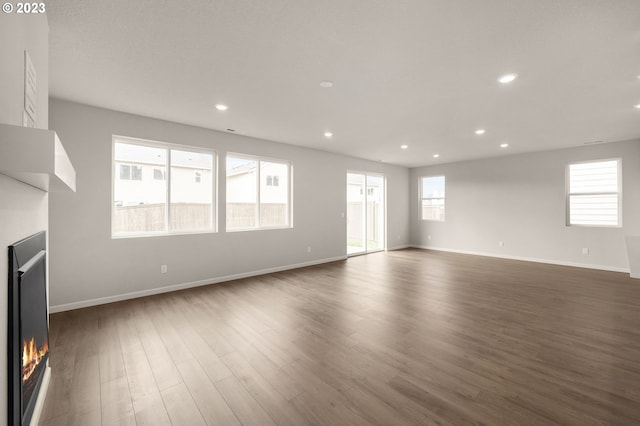 unfurnished living room with a lit fireplace, baseboards, dark wood-style flooring, and recessed lighting