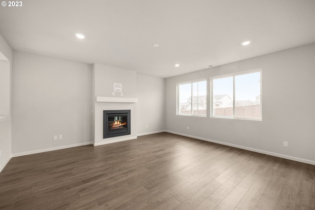 unfurnished living room featuring baseboards, dark wood-type flooring, a glass covered fireplace, and recessed lighting