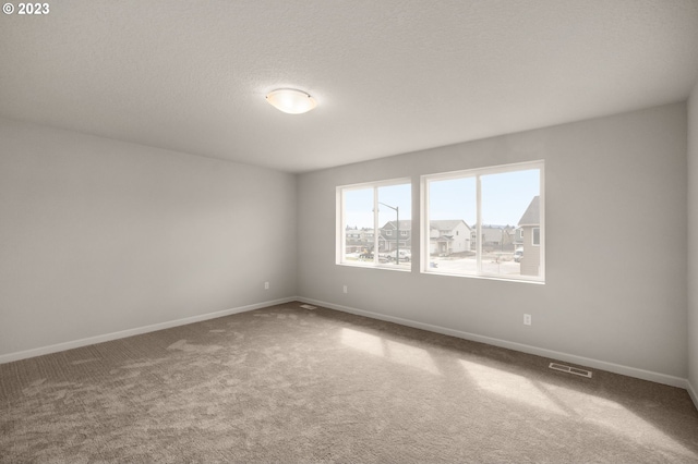 carpeted spare room featuring baseboards, visible vents, and a textured ceiling