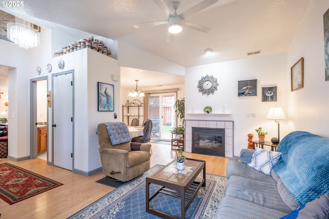 living room featuring a tiled fireplace, lofted ceiling, light hardwood / wood-style flooring, and ceiling fan with notable chandelier