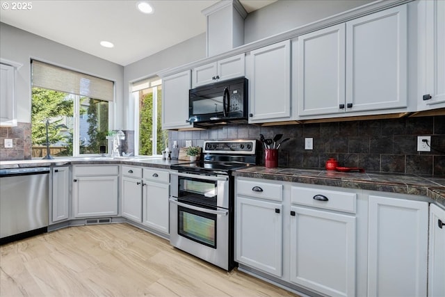 kitchen with white cabinets, backsplash, appliances with stainless steel finishes, and light wood-type flooring