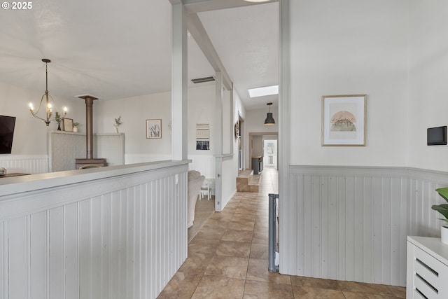 hallway with visible vents, a notable chandelier, and wainscoting