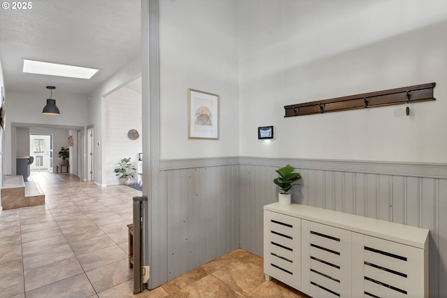 corridor featuring a skylight, a wainscoted wall, and light tile patterned flooring