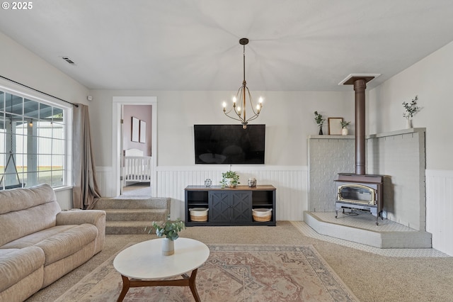 carpeted living area featuring a wood stove, a wainscoted wall, stairway, and visible vents