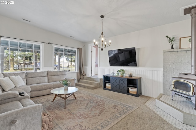 living room featuring a wainscoted wall, lofted ceiling, visible vents, a wood stove, and a chandelier