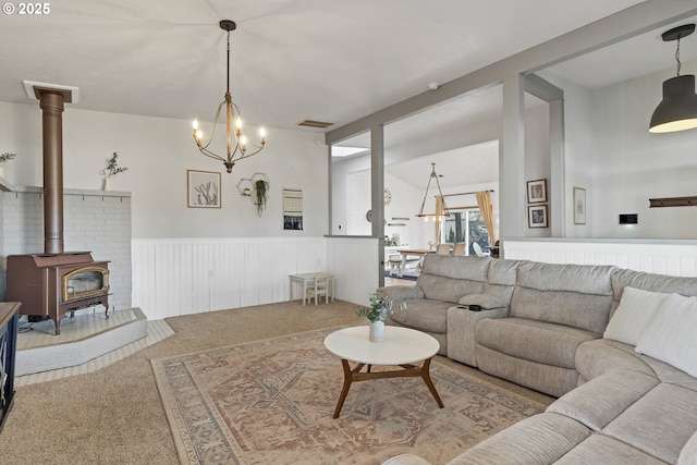 carpeted living room featuring a wood stove, wainscoting, vaulted ceiling, and visible vents