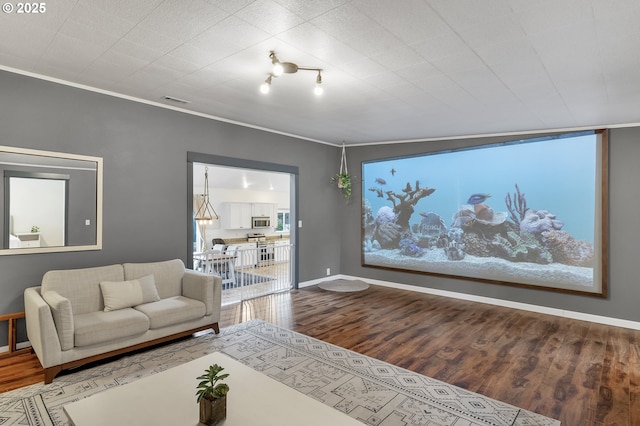 living area with wood finished floors, visible vents, baseboards, a healthy amount of sunlight, and crown molding