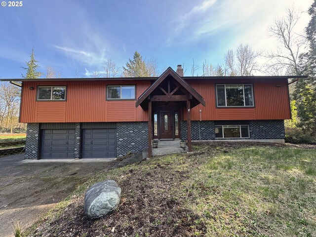 raised ranch featuring driveway, a front yard, a garage, brick siding, and a chimney