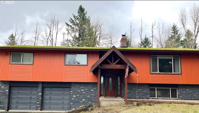 bi-level home with brick siding, driveway, a chimney, and a garage