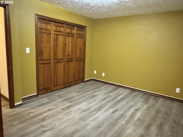 unfurnished bedroom featuring baseboards, light wood-type flooring, a closet, and a textured ceiling