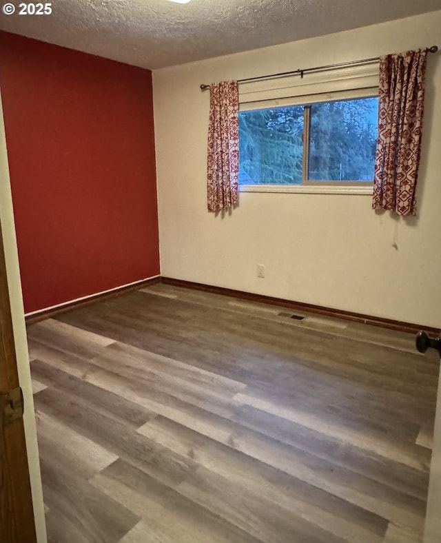 unfurnished room with baseboards, a textured ceiling, and wood finished floors