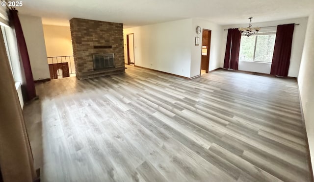 unfurnished living room with a fireplace, a notable chandelier, wood finished floors, and baseboards