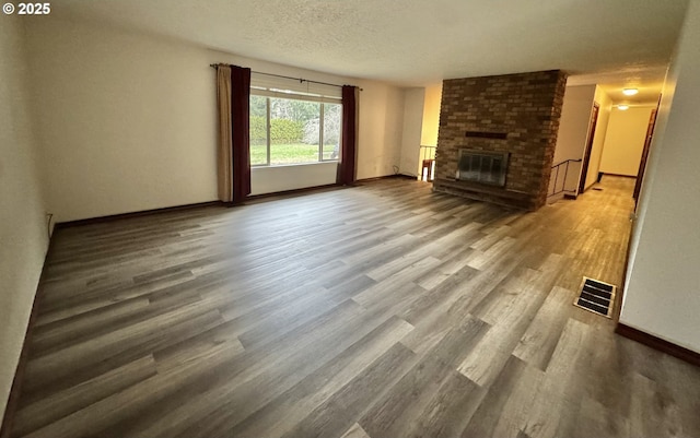 unfurnished living room with visible vents, baseboards, a fireplace, wood finished floors, and a textured ceiling