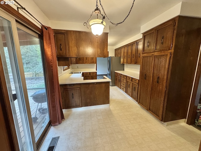 kitchen featuring visible vents, freestanding refrigerator, a peninsula, light countertops, and light floors