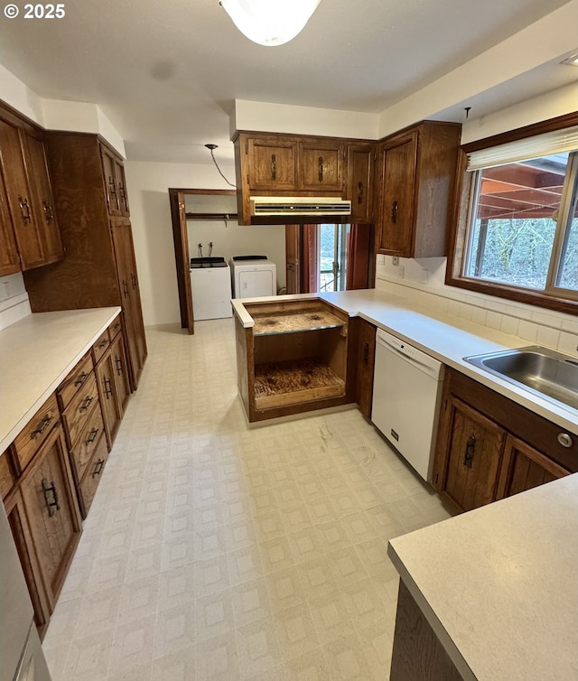 kitchen featuring under cabinet range hood, light countertops, light floors, dishwasher, and washing machine and clothes dryer