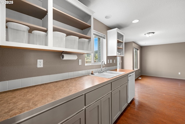 kitchen with a sink, gray cabinets, wood finished floors, open shelves, and dishwasher