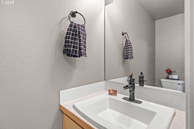half bath featuring vanity, toilet, and a textured wall