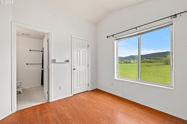 unfurnished bedroom featuring lofted ceiling, ensuite bath, visible vents, light wood finished floors, and baseboards