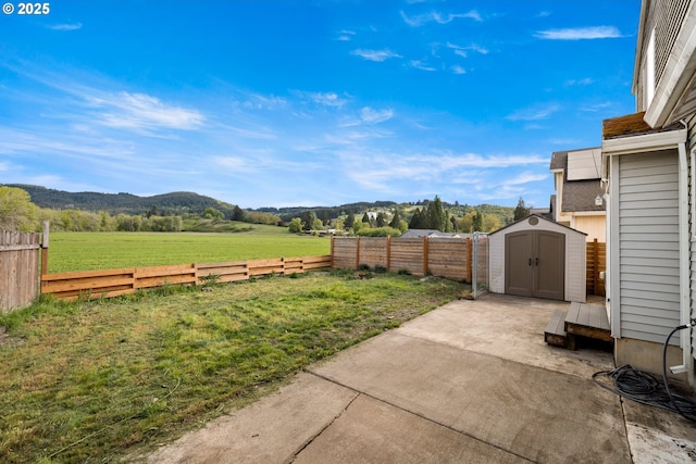 view of yard with a mountain view, a patio, an outdoor structure, a fenced backyard, and a shed