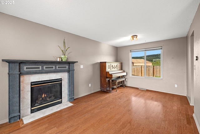 living room featuring baseboards, a tile fireplace, visible vents, and wood finished floors