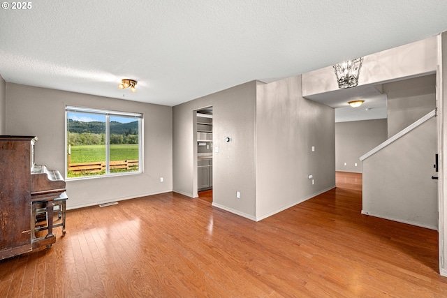 unfurnished living room with stairs, baseboards, visible vents, and wood finished floors