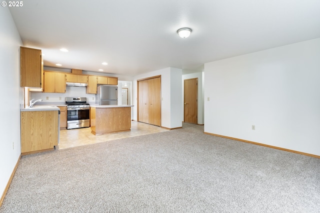 kitchen with light colored carpet, stainless steel appliances, a sink, open floor plan, and light countertops