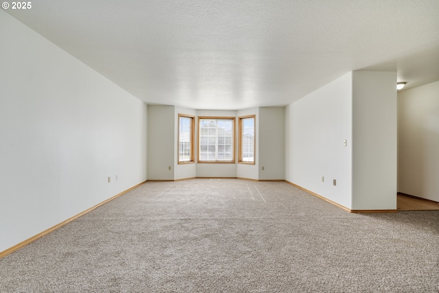 spare room featuring light colored carpet, a textured ceiling, and baseboards