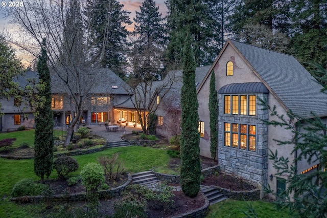 1500 SE Waverly Dr, Milwaukie, OR 97222 - back of property at dusk featuring stucco siding, stone siding, a lawn, and a patio area