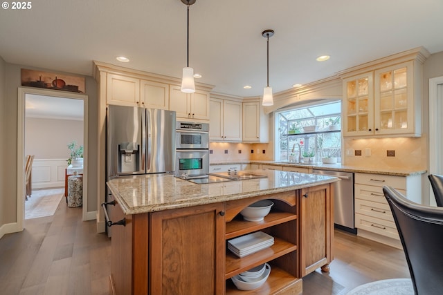 kitchen with sink, hanging light fixtures, stainless steel appliances, a center island, and light stone countertops