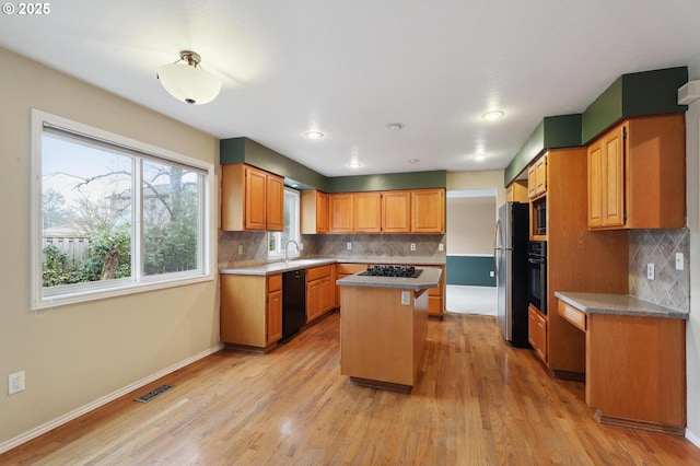 kitchen featuring a kitchen island, tasteful backsplash, sink, light hardwood / wood-style floors, and black appliances