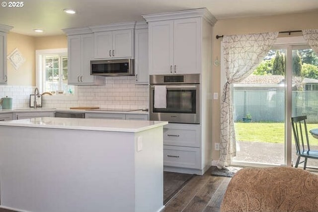 kitchen featuring stainless steel appliances, a sink, light countertops, dark wood-style flooring, and tasteful backsplash