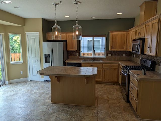 17458 SW Inkster Dr, Sherwood, OR 97140 - kitchen featuring appliances with stainless steel finishes, tile countertops, decorative backsplash, a kitchen island, and hanging light fixtures