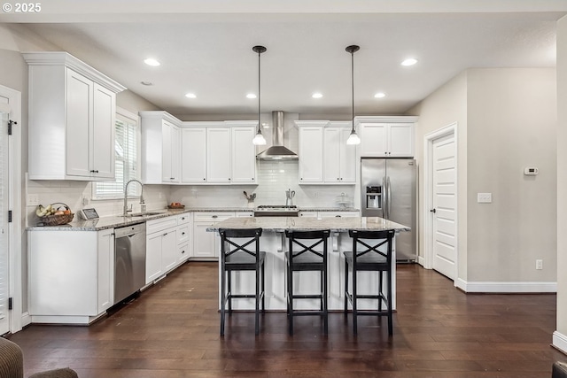 kitchen with wall chimney exhaust hood, decorative light fixtures, a center island, appliances with stainless steel finishes, and light stone countertops