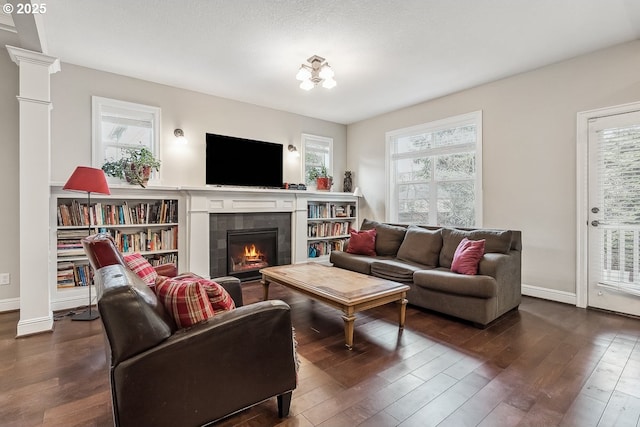 living room featuring dark hardwood / wood-style floors, a tile fireplace, and ornate columns