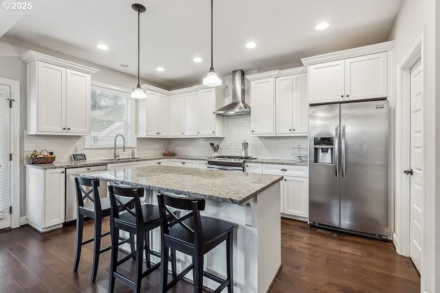 kitchen featuring appliances with stainless steel finishes, sink, white cabinets, hanging light fixtures, and wall chimney exhaust hood