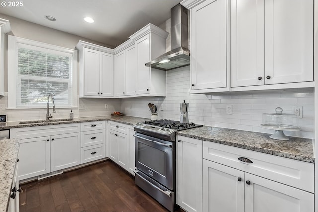 kitchen with white cabinetry, sink, light stone counters, stainless steel gas range, and wall chimney exhaust hood