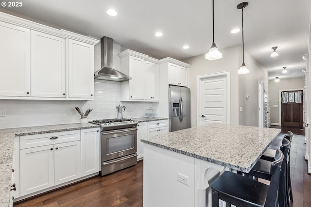 kitchen featuring appliances with stainless steel finishes, pendant lighting, white cabinets, light stone counters, and wall chimney exhaust hood