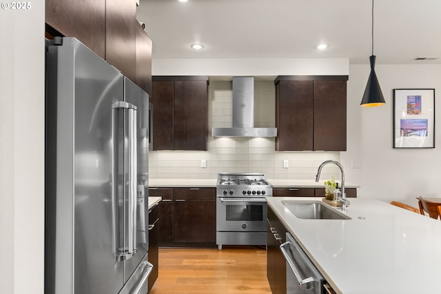 kitchen with sink, light wood-type flooring, pendant lighting, premium appliances, and wall chimney exhaust hood