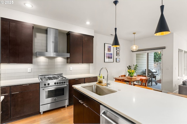 kitchen with stainless steel appliances, sink, dark brown cabinets, wall chimney exhaust hood, and pendant lighting