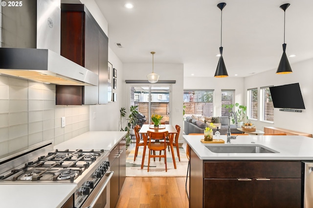 kitchen featuring a center island with sink, sink, stainless steel appliances, and wall chimney range hood