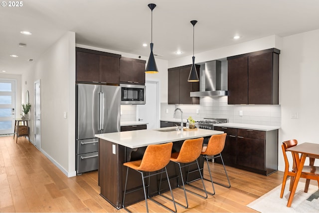 kitchen with sink, pendant lighting, high end fridge, built in microwave, and wall chimney exhaust hood