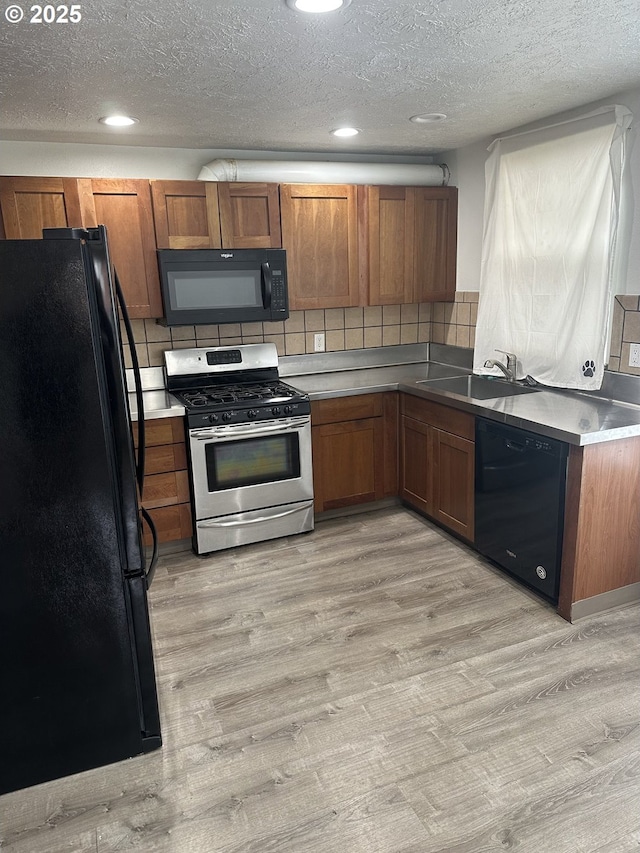 kitchen featuring black appliances, brown cabinetry, light wood-style floors, and a sink