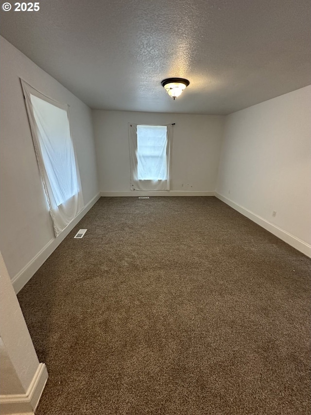 empty room featuring baseboards, visible vents, dark colored carpet, and a textured ceiling