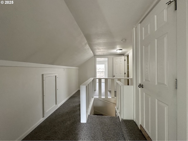 hall with vaulted ceiling and dark colored carpet