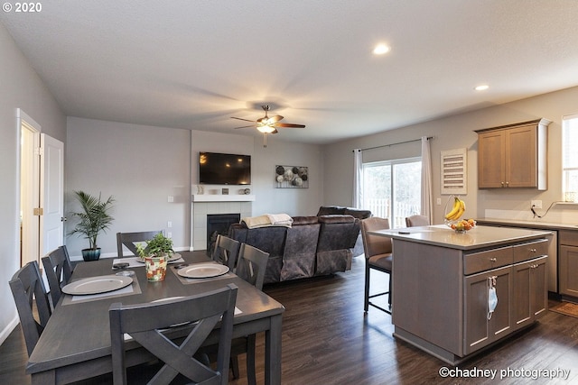 dining area with dark wood-style floors, a ceiling fan, a tiled fireplace, and recessed lighting