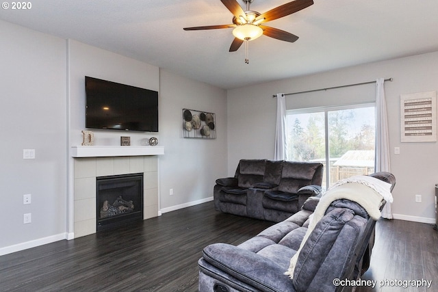 living room with baseboards, a fireplace, a ceiling fan, and dark wood-type flooring