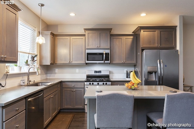 kitchen featuring appliances with stainless steel finishes, dark wood-style flooring, hanging light fixtures, light countertops, and a sink