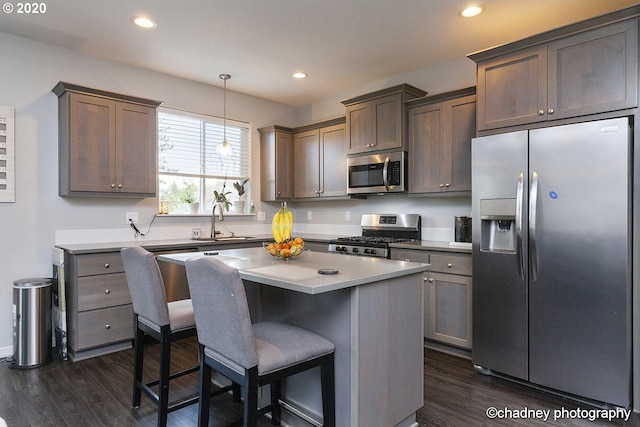 kitchen featuring light countertops, hanging light fixtures, appliances with stainless steel finishes, a sink, and a kitchen island