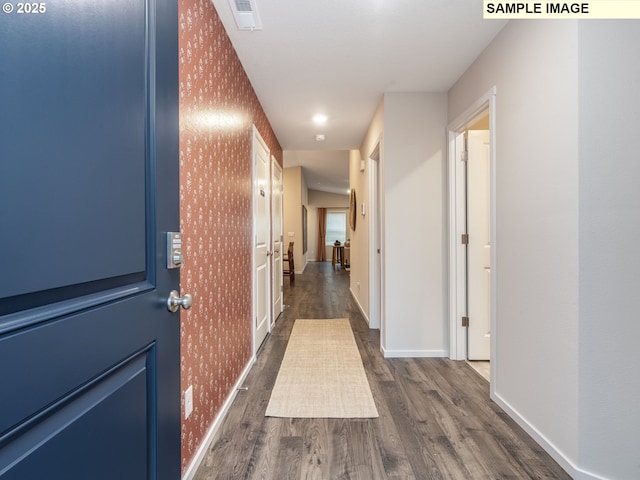 hallway with visible vents, baseboards, wallpapered walls, dark wood-type flooring, and an accent wall