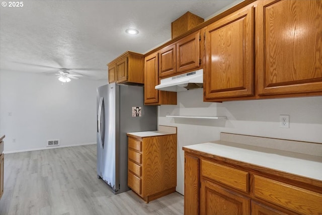 kitchen with under cabinet range hood, brown cabinets, ceiling fan, light countertops, and light wood-style floors